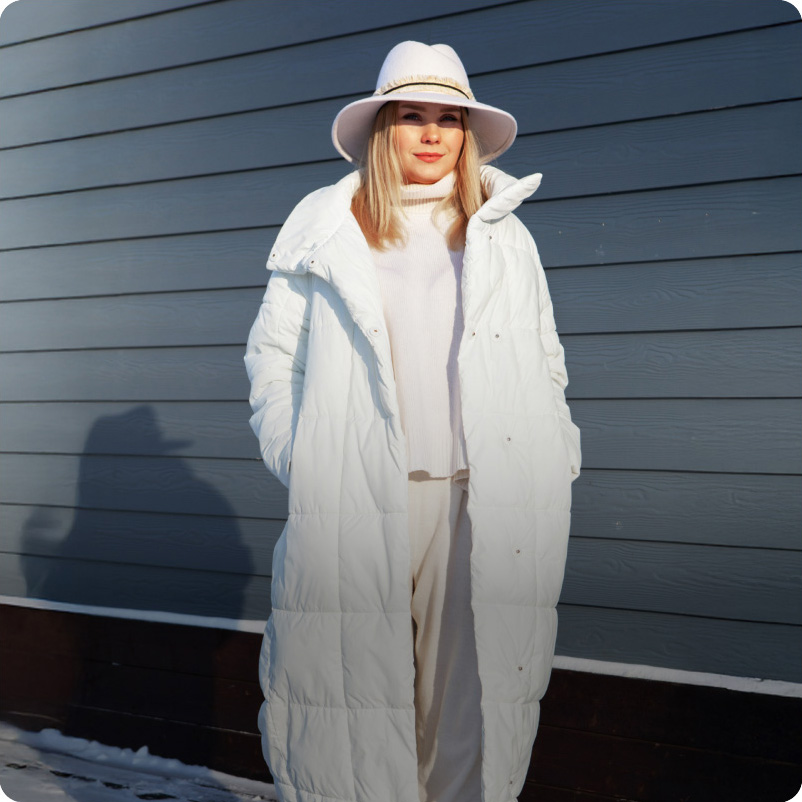 Woman staying warm on a windy day in a shiny black puffer jacket with comfortemp® insulation, under a cloudy blue sky.